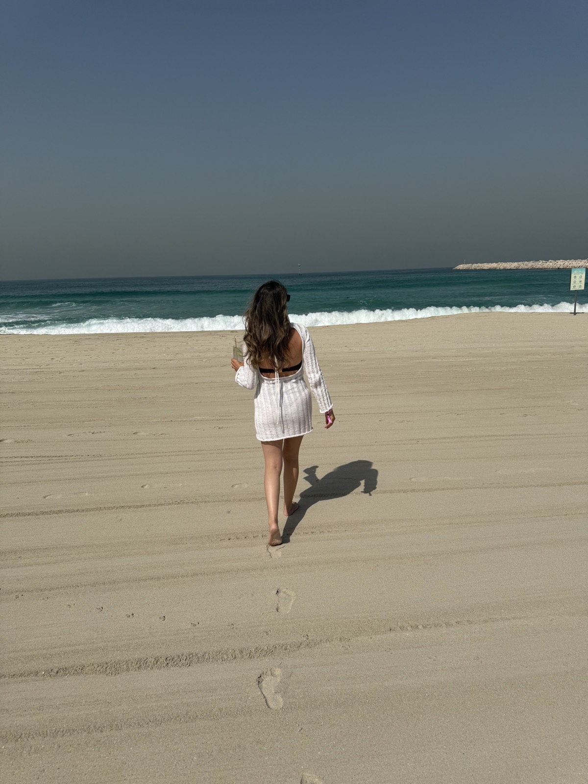 Walking barefoot across the sand towards the sea at Kite Beach, Dubai, coffee in hand