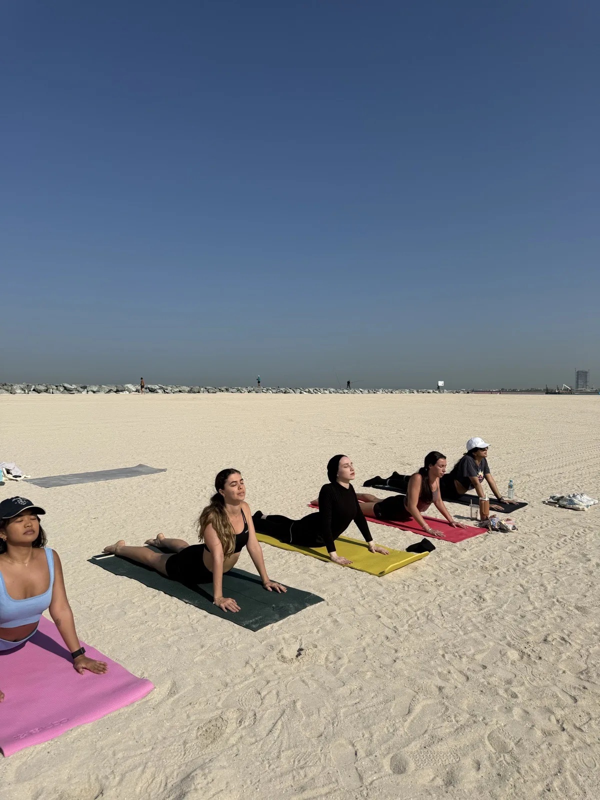 Beach Pilates class moving through a spinal extension exercise on mats on the sand