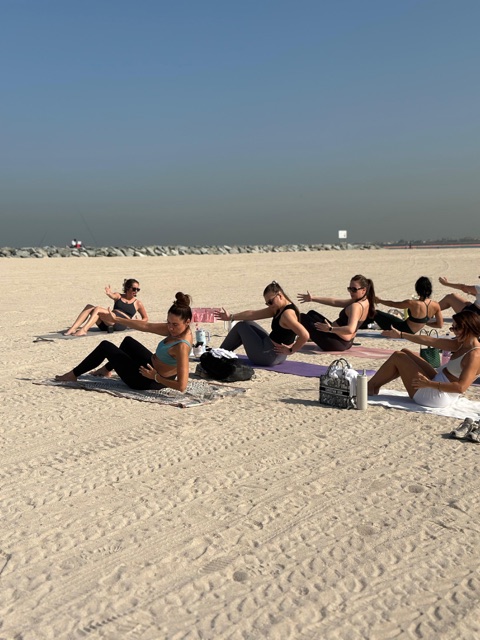 Beach Pilates class practising seated oblique twists on the sand
