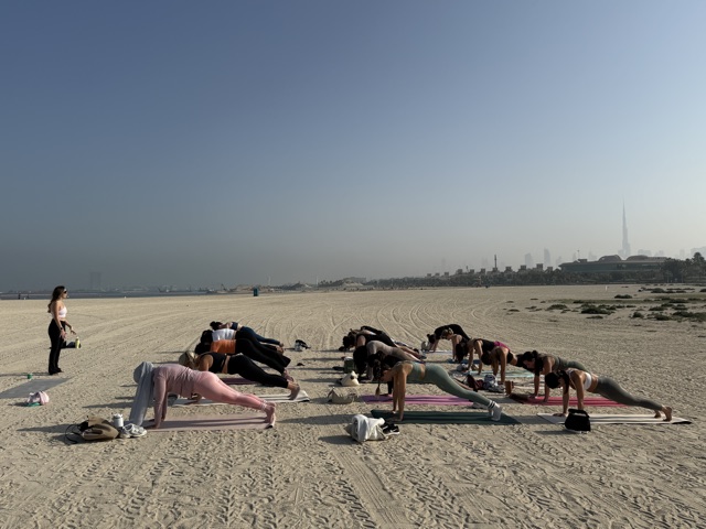 Beach Pilates class holding plank position in a row facing the Dubai skyline