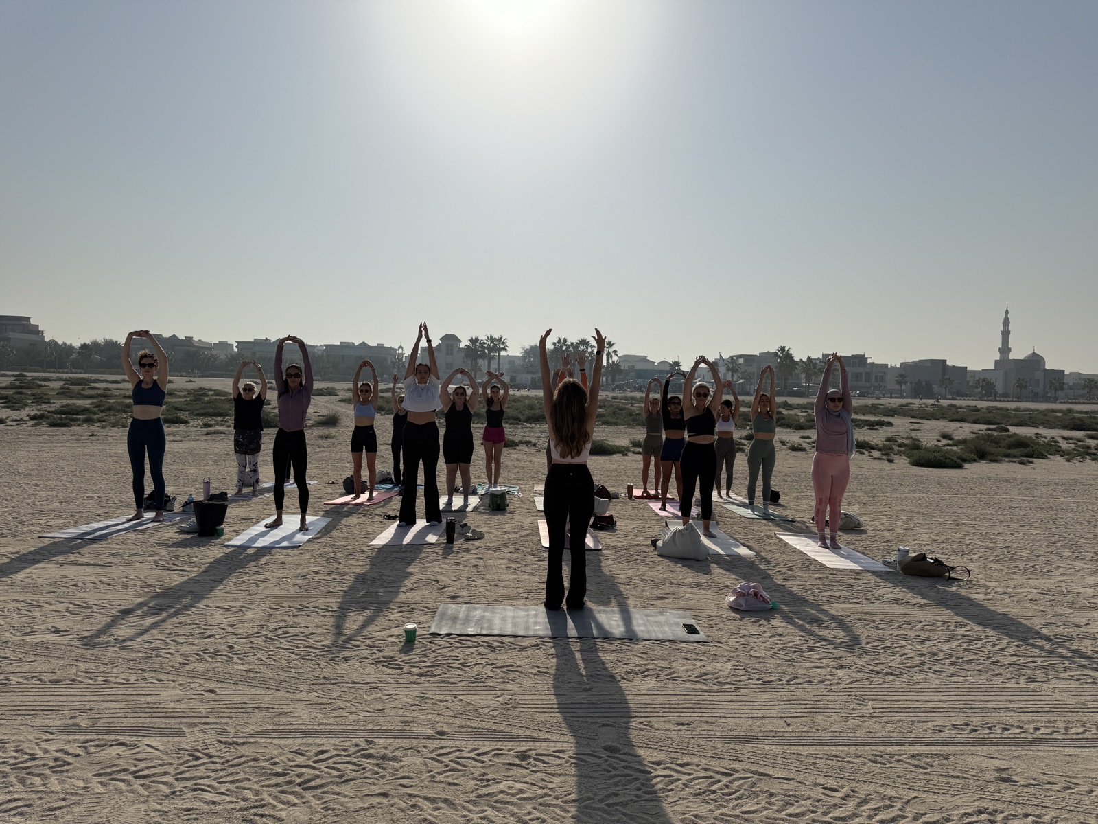 Sunrise beach Pilates class reaching overhead as the sun rises over the Dubai skyline