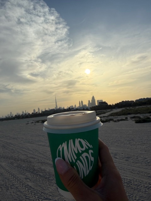 Takeaway coffee held up against the sunrise over the Dubai skyline after a beach Pilates class