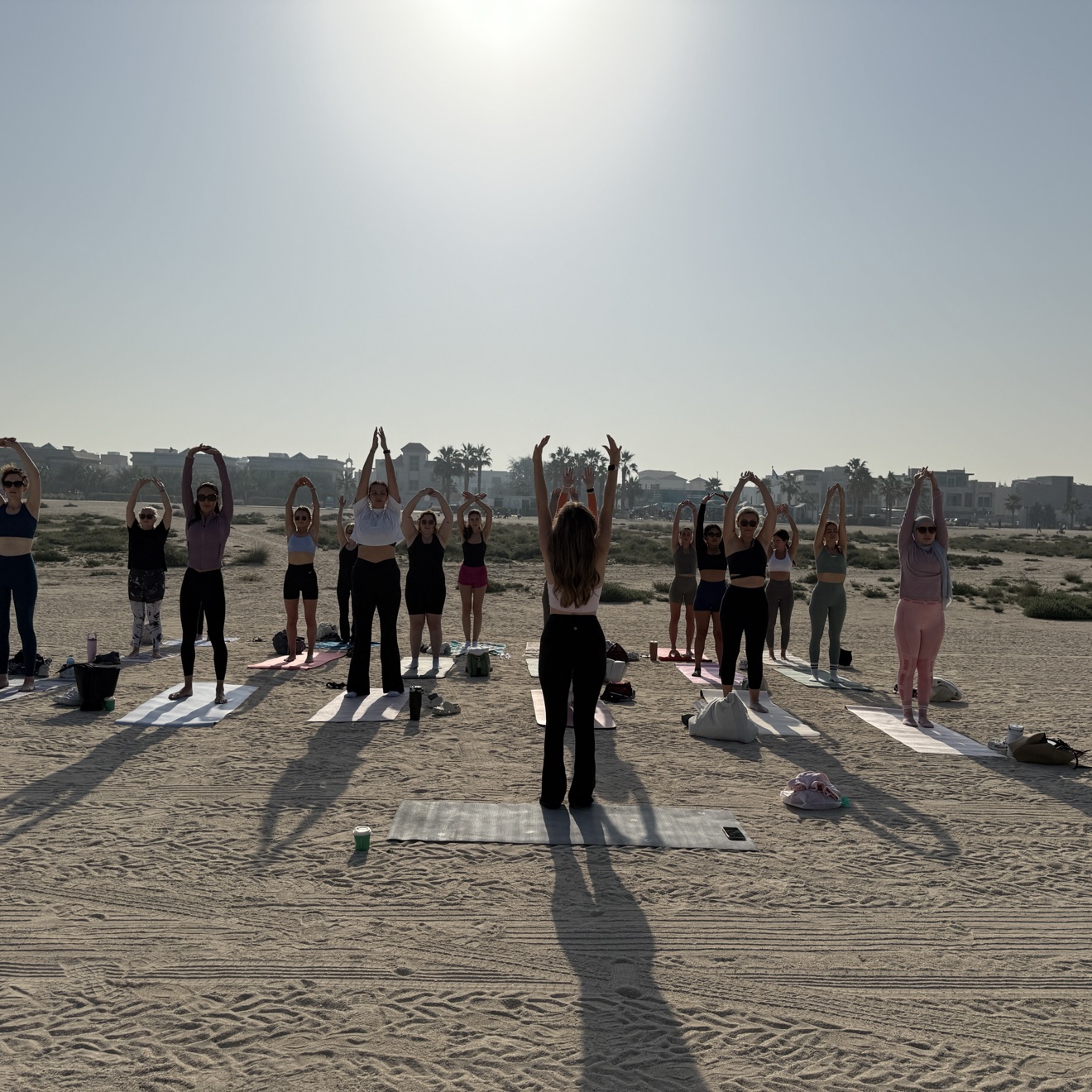 A sunrise beach Pilates class at Kite Beach, Dubai, the whole group stretching arms overhead